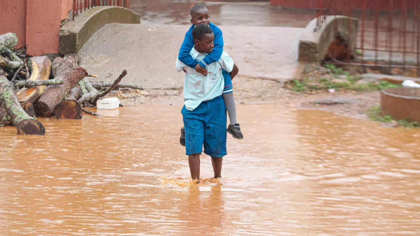 A boy carrying a younger child on his back through a flooded street